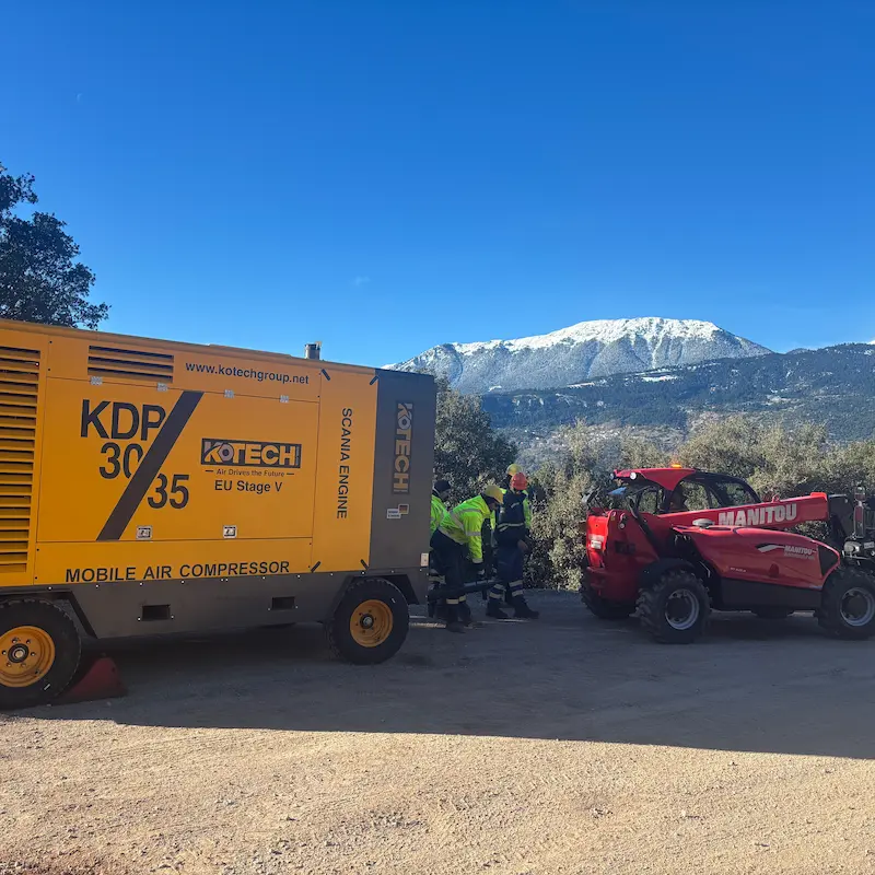 Kotech KDP-30/25 diesel portable air compressor operating alongside a DTH drilling rig at an open-pit iron ore mine in South Africa.