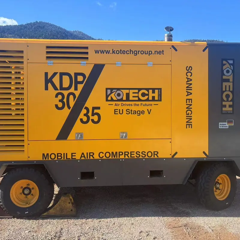 Kotech KDP-30/25 diesel portable air compressor operating alongside a DTH drilling rig at an open-pit iron ore mine in South Africa.